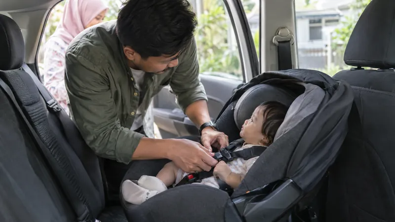 Illustration: a father checking the harness of an infant car seat in a car's back seat