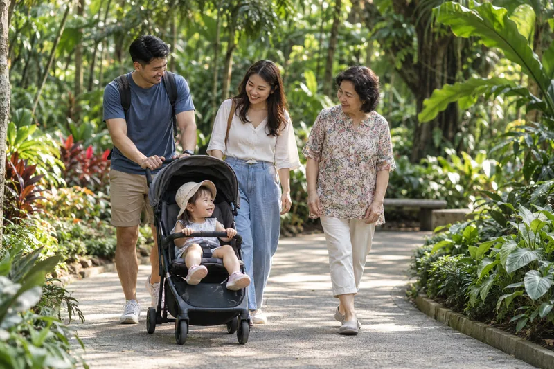 Keluarga pelbagai generasi berjalan di laluan taman tropika yang teduh