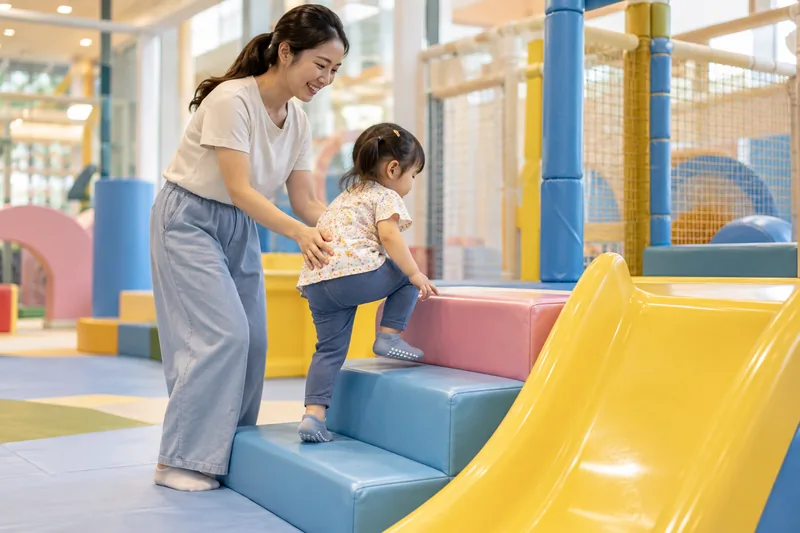 Ibu atau bapa menemani anak kecil di kawasan permainan dalaman beralas lembut