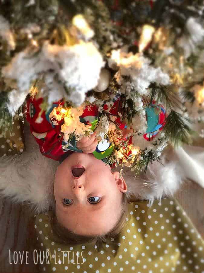 Baby peeking out from under a Christmas tree with cute "open-mouth" expression.