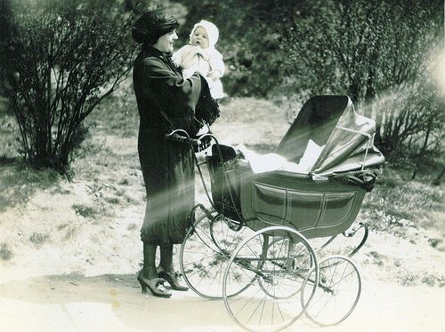  A woman carrying a baby posing near a 1920s stroller - When Were Strollers Invented History of Baby Strollers – Baby Journey