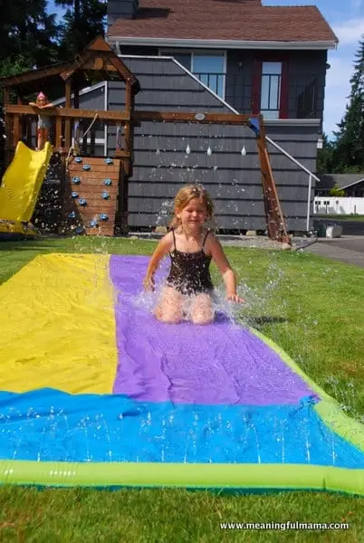 A young girl playing with Slip ‘N Slide water obstacle course while playing backyard obstacle course for toddlers - Best Toddler Obstacle Course Ideas to Build Your Child's Gross Motor Skills - Baby Journey