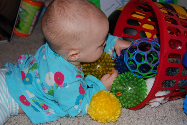 Cute baby grabbing toys from a textured toy bin - Simple Gross Motor Activities for Infants - Baby Journey