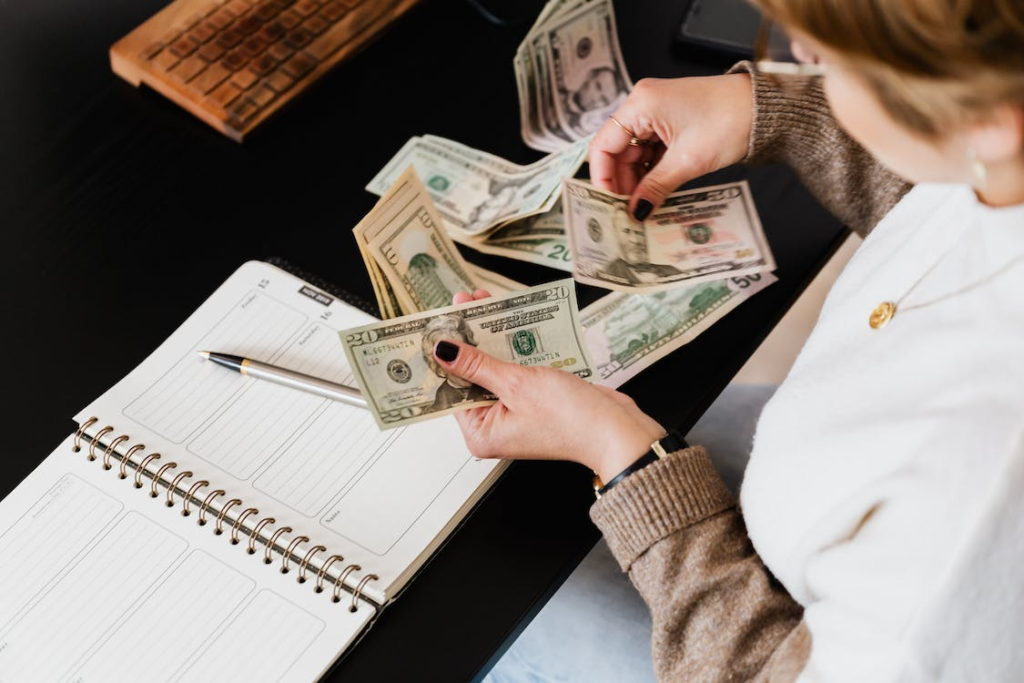 Unknown lady counting her money to mange and organize her finances with a notebook on table - How To Prepare Financially When You're Expecting A Child - Baby Journey