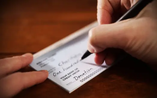 Unknown hand writing a check for donation to charities for autism - How to get involved with autism charities - Baby Journey
