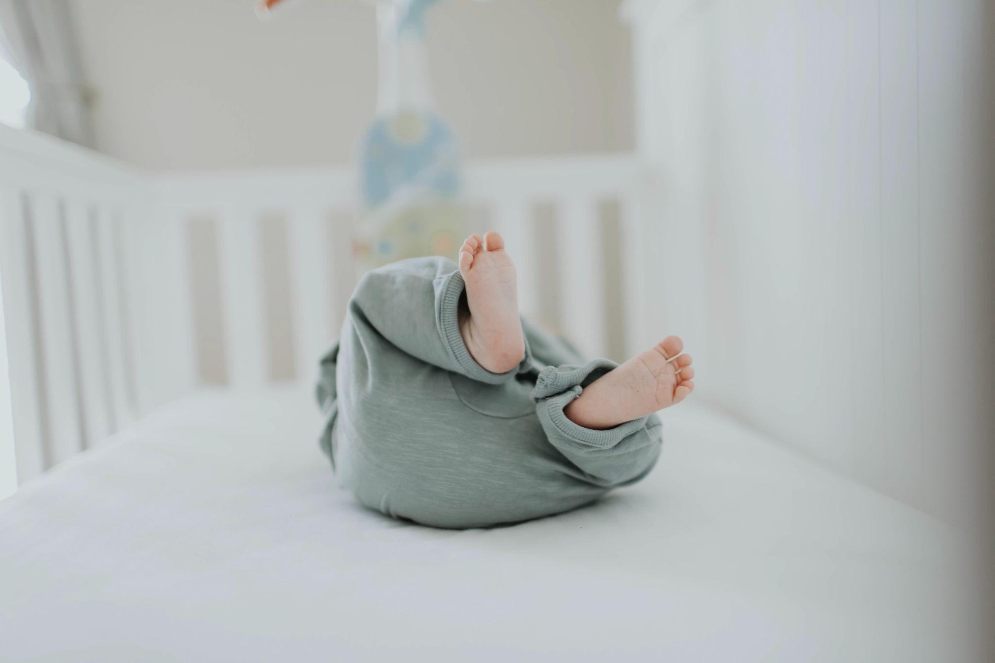 Picture of a baby’s butt and feet facing the camera while baby is lying in crib - How to Make Baby More Comfortable in Crib - Baby Journey