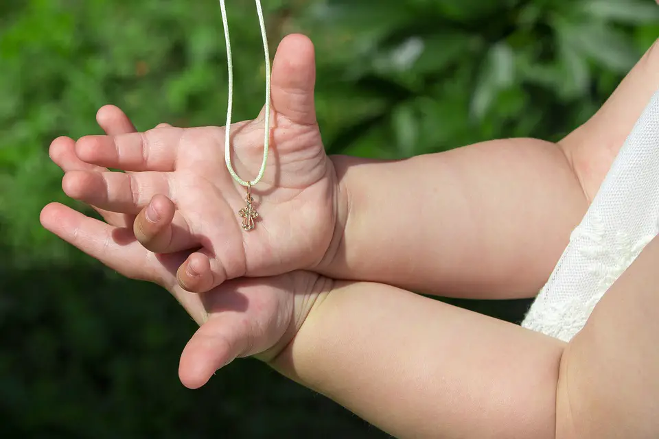 Small child’s hands holding a baptism necklace gift - Baby dedication vs baptism - Baby Journey