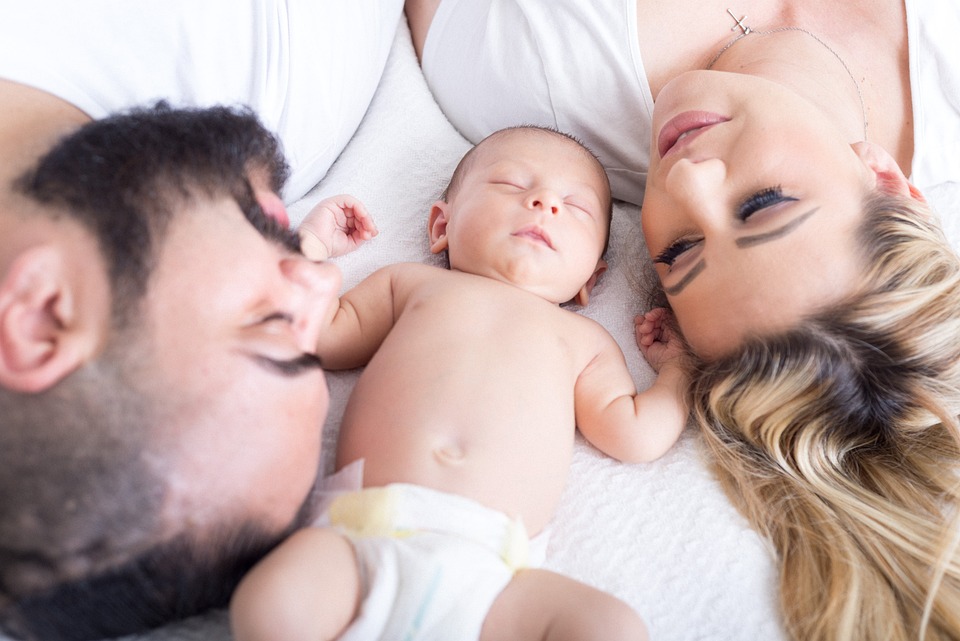 A couple laying on the bed while looking at their sleeping baby boy - Catholic baby names - Baby Journey