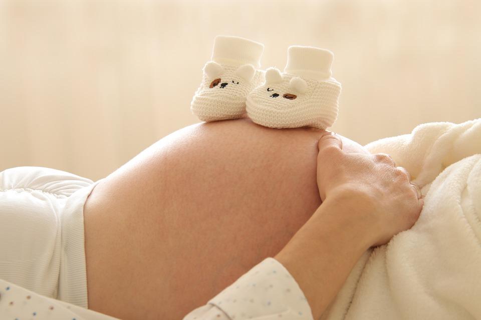 A pair of white baby booties resting on a pregnant mother’s belly - Catholic baby names - Baby Journey