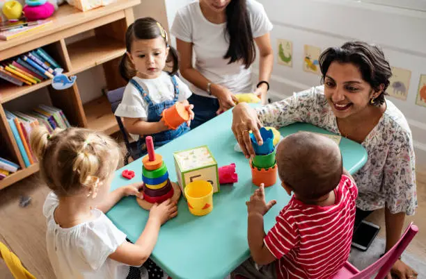 A daycare teacher interacting with young nursery children at early learning centre nursery playroom - Benefits of early childhood education - Baby Journey