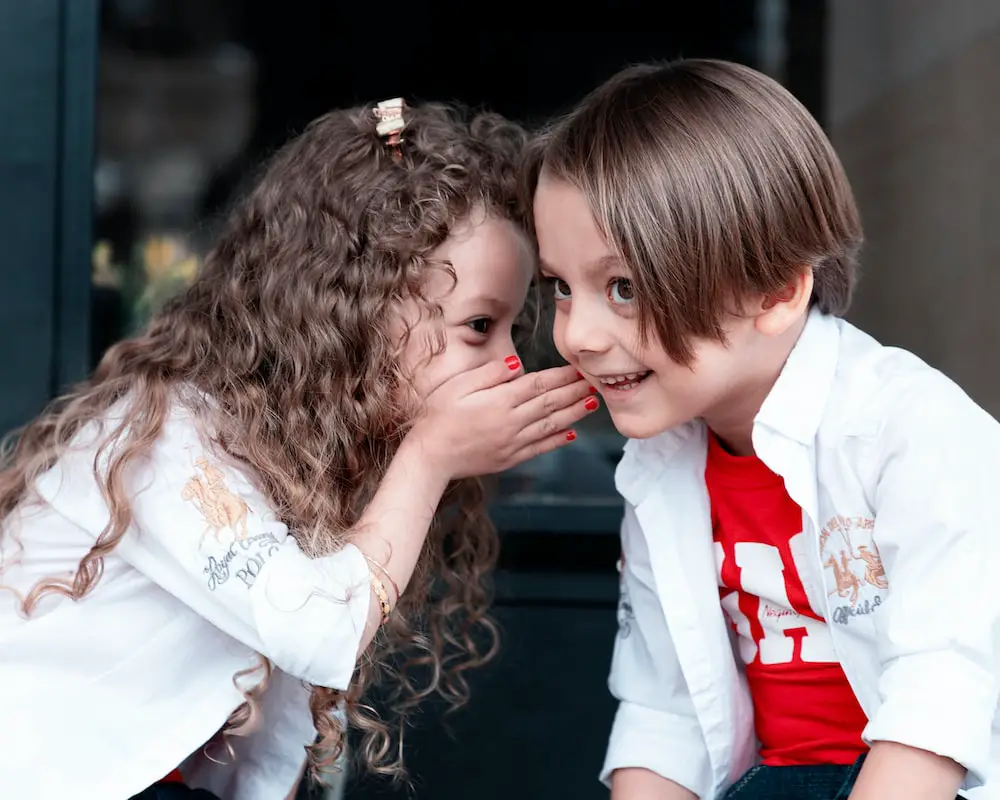 A young girl whispering to a young boy kids model pictures - kids modeling career - Baby Journey
