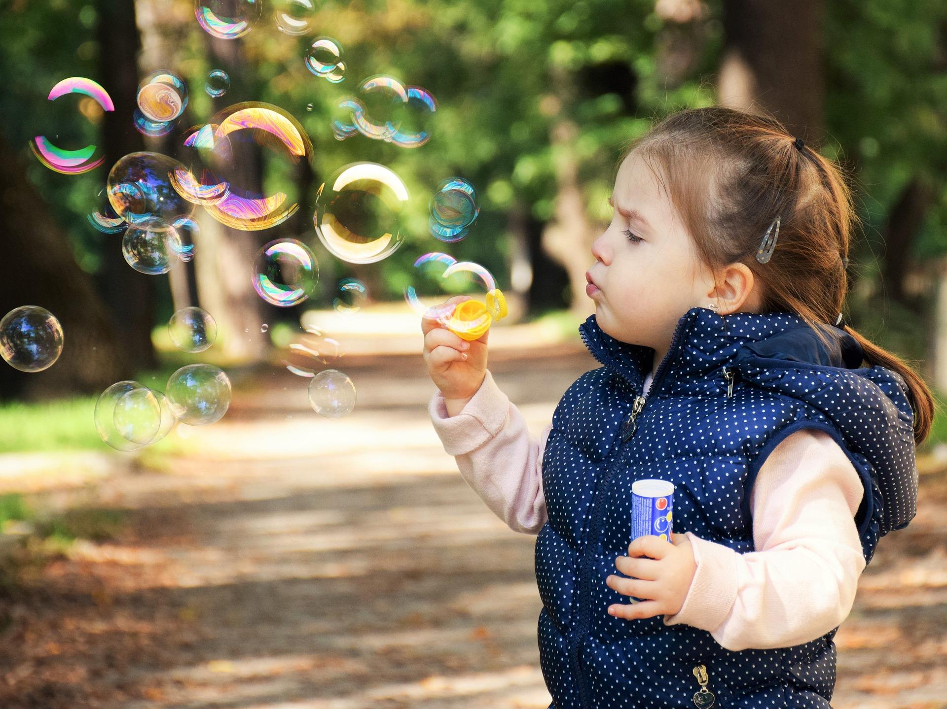 A little girl blowing bubbles in a park - Adopting a newborn vs adopting a toddler - Baby Journey