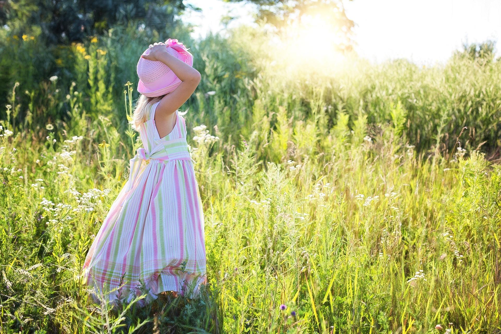 A young girl wearing a pink hat and striped dress standing in a field - Toddler adoption vs newborn adoption - Baby Journey