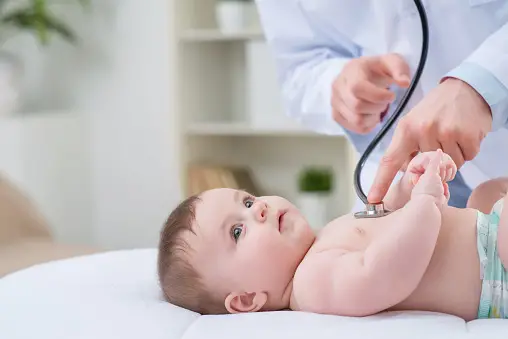  Baby lying down on bed while a doctor checks on him - Why Do Babies Slobber - Baby Journey