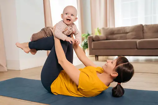 Mother holding a baby while exercising after giving birth - What are the Benefits of Postpartum Exercises - Baby Journey