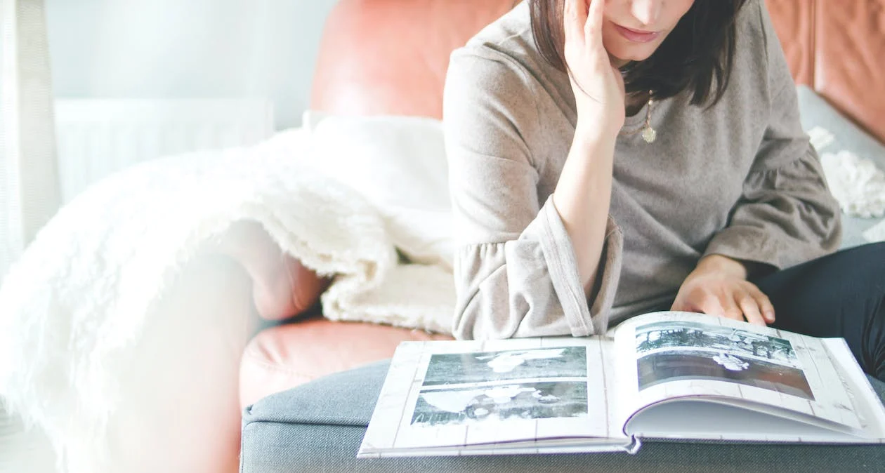 A woman sitting on a sofa looking through bridal shower photoshoot photo album - Should You Hire the Same Photographer for Your Bridal Shower Photography and Baby Shower - Baby Journey