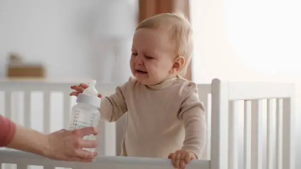 Baby crying and handing over milk bottle to parent- Why Does My Baby Cry While Eating Formula - Baby Journey