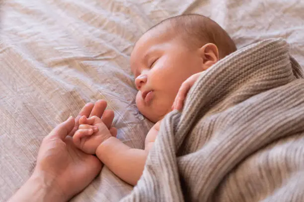 Parents holding the hand of a sleeping baby - How to Keep Babies Hands Warm at Night - Baby Journey