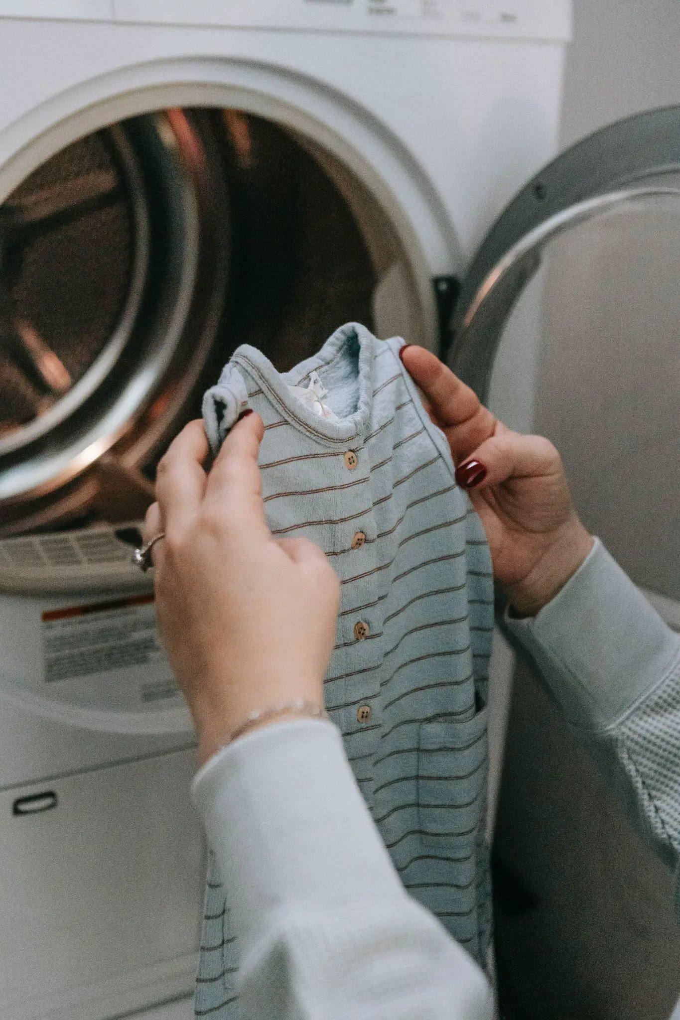 A mom picks up washed baby clothes in front of the washing machine - How to Wash Baby Clothes - Baby Journey