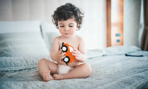 Baby playing with a toy car on the bed - Why Does My Baby Keep Getting Ear Infections - Baby Journey