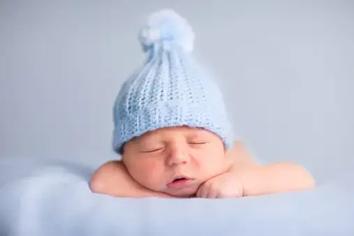 Cute newborn baby wearing a blue hat sleeping on a blue surface - Best Names That Mean Blue for Girls and Boys - babyjourney.net