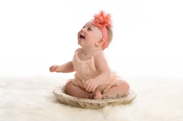 Cute baby girl dressed in sexy dress and orange pink headband sitting in a wooden bowl - 550+ Sexy Girl Names - babyjourney.net