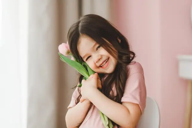 Cute little girl holding a flower and smiling - 230+ Ethereal Names for Girls and Boys - babyjourney.net