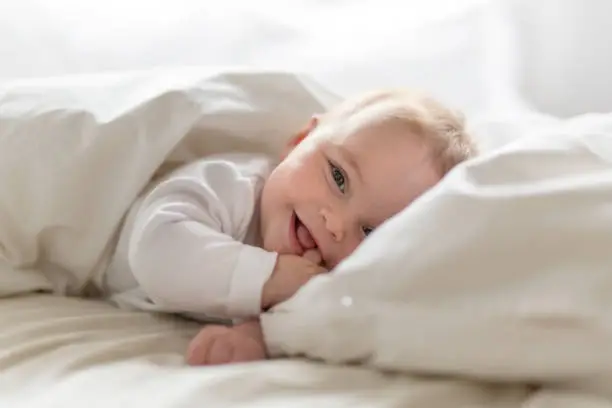 Photo of smiling baby in bed - Steps to Take If Your Child Has Been Affected by NEC Baby Formula - babyjourney.com Parenting Blog